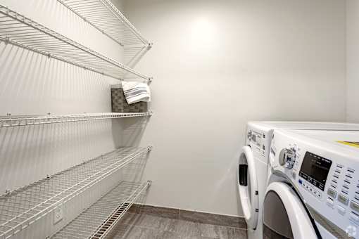 A white washing machine sits next to a metal shelf with a towel on it at Saba Pompano Beach, Pompano Beach, 33062