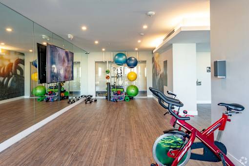 A red exercise bike is in a room with a mirrored wall and exercise balls at Saba Pompano Beach, Pompano Beach, 33062