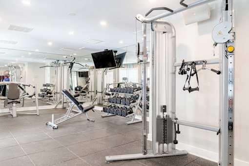 A gym with a variety of equipment including a weight bench, a cable machine, and a flat screen TV.