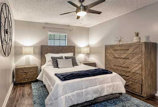 2-Bedroom Apartments in Riverview, FL - Sherwood Oaks Apartments - Cozy Bedroom With Wood Bed Frame, Ceiling Fan Light, Matching Nightstands, Textured Rug, and Chevron Front Dresser.