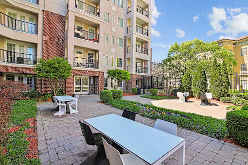 Atlanta, GA, Luxury Apartments Near Lenox Square - The Rocca - A Patio with Tables and Chairs and Paved Walkways Lined with Shrubs.