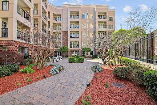 A brick walkway leads to a courtyard with a fence and trees.