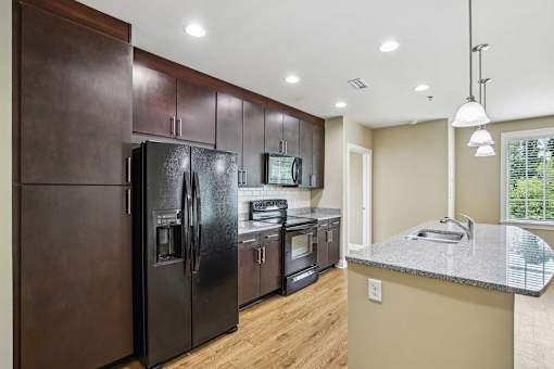 Atlanta, GA, Luxury Apartments Near Chastain Park - The Rocca - A Kitchen with Dark Cabinetry, Black Appliances, and a Spacious Granite Countertop Island.