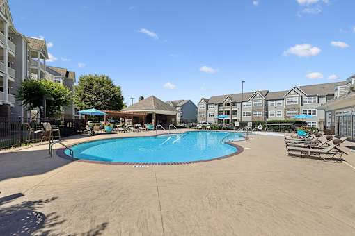 A large swimming pool surrounded by a sandy area and chairs.