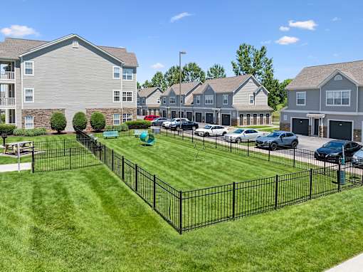 A black fence surrounds a green lawn in front of apartment buildings.