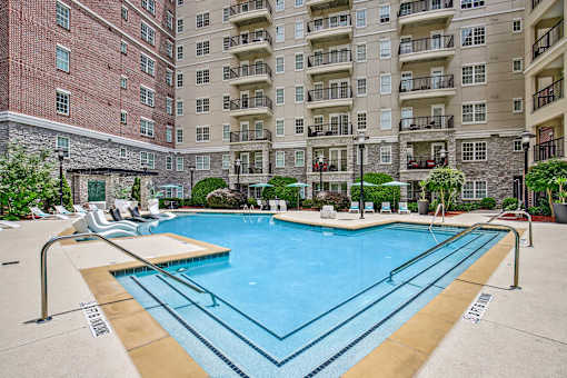 Atlanta, GA, Luxury Apartments Near Phipps Plaza - The Rocca - A Swimming Pool Surrounded by Lounge Chairs, Umbrellas, and a Multi-Story Apartment Building.
