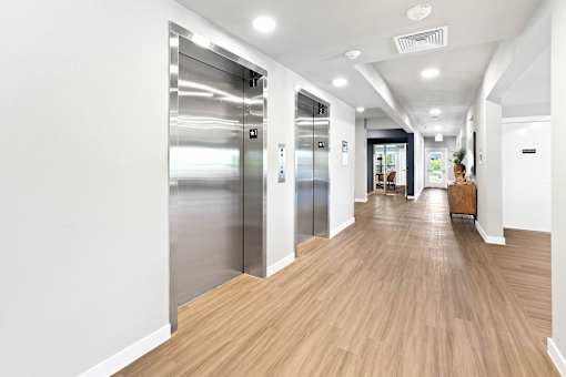 A long hallway with wood floors and two elevators.