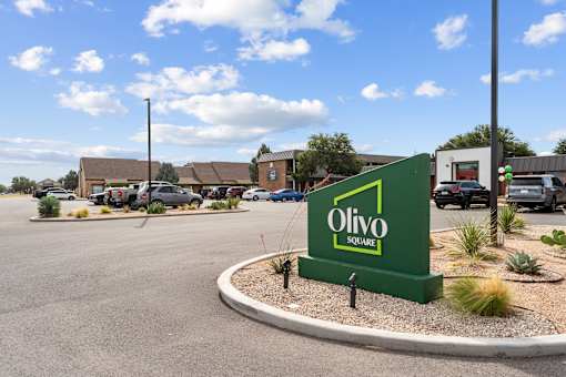 A green sign that says Olivo Square is in front of a parking lot.