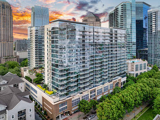 A modern glass building is surrounded by other buildings and trees.