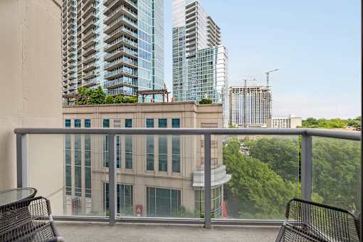A balcony with a table and chairs overlooks a cityscape with modern buildings.