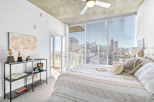A bedroom with a large bed and a city view through the window.