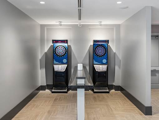 Two vending machines with a blue and red design are in a hallway with wooden floors.