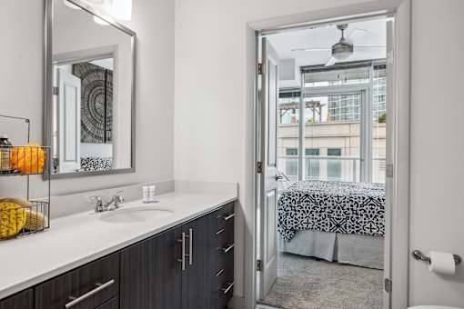A bathroom with a mirror, sink, and a view of a bedroom through an open door.