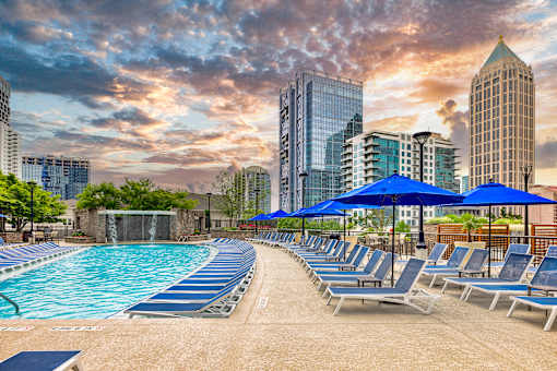 A pool with blue umbrellas and chairs in front of a city skyline.
