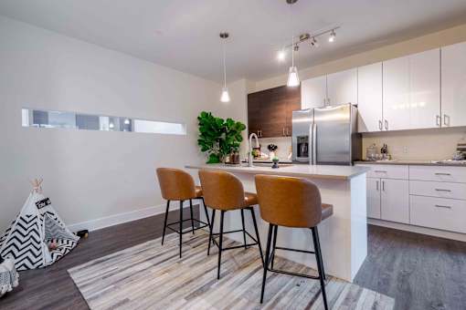 Studios in Tampa, FL - Society Westshore - Kitchen with Wood Plank Style Flooring, Large Island with Seating, Pendant Lights, Quartz Countertops, Stainless Steel Appliances, and Flat-Panel Cabinetry.