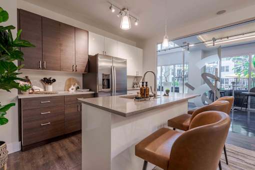 2-Bedroom Apartments in Tampa, FL - Society Westshore - Kitchen with Wood Plank Style Flooring, Large Island with Seating, Pendant Lights, Quartz Countertops, Stainless Steel Appliances, and Flat-Panel Cabinetry.