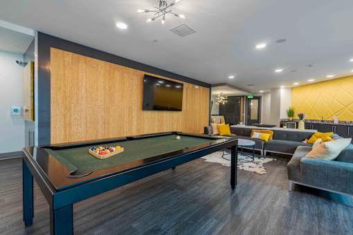 A pool table is in the middle of a room with a couch and a TV mounted on the wall.