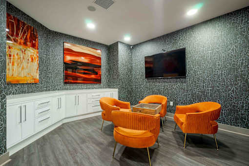 A room with orange chairs and a television on the wall.
