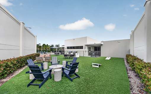 A white building with a green lawn in front and blue chairs.