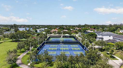 A tennis court surrounded by greenery and buildings.