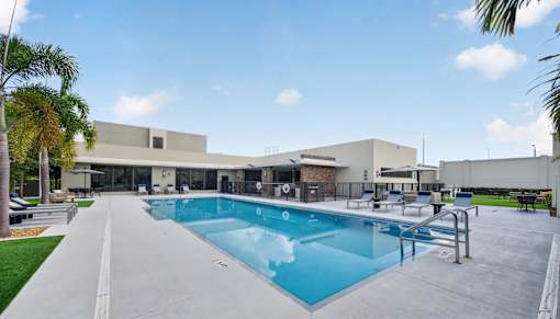 A large swimming pool is surrounded by a concrete patio and a building.