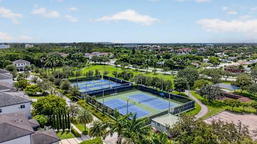 A tennis court surrounded by greenery and residential houses.