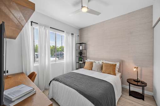A bedroom with a bed, a chair, a table, and a ceiling fan.