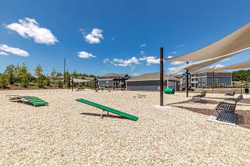 A playground with a green bench and a shade structure.