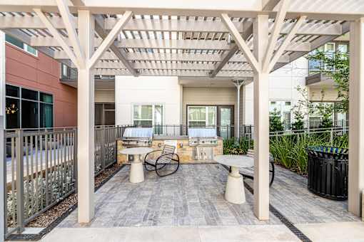 Pet-Friendly Luxury Apartments in Fort Worth, TX - The Union at River East - Grilling Station Underneath a Wooden Pergola, with Two Built-In Stainless Steel Grills, Tables, Armchairs, and a Trash Bin.