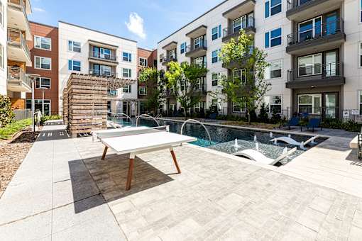 A table tennis table is in the middle of a courtyard with a pool.