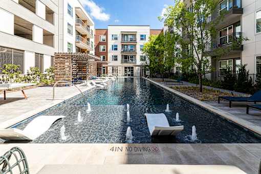 Two-Bedroom Luxury Apartments in Fort Worth, TX - The Union at River East - Swimming Pool with Small Fountains, In-Pool Loungers, Sun Loungers, Pergolas, Trees, and Metal Fence.