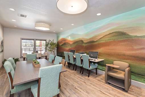A room with a mural of a landscape on the wall and several chairs and tables.