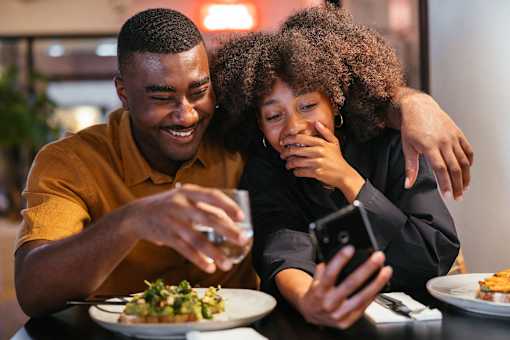 a man and woman sitting at a restaurant table looking at a cell phone
