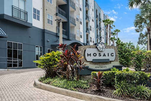 A sign for Mosaic Apartments is in front of a building with a landscaped area.