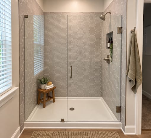 A bathroom with a white shower stall and a small wooden table with a plant on it.