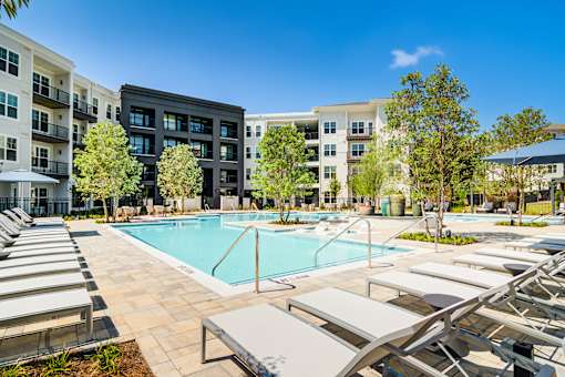 Pet-Friendly Luxury Apartments in Sugar Hill, GA - The Collier Sugar Hill - Large Resort-Style Heated Pool Surrounded by Loungers, Umbrellas, Cabanas, Trees, and Apartment Buildings.