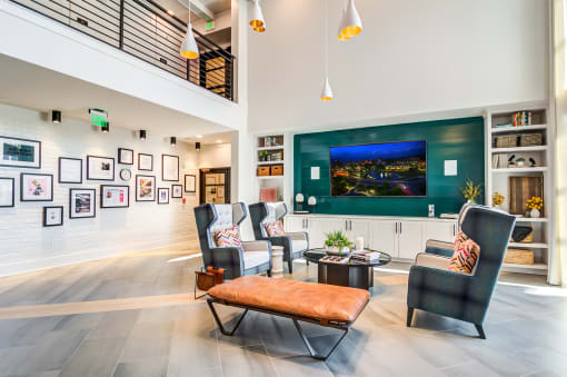 Huntsville, AL Luxury Apartments - The Collins - Clubhouse with Wingback Armchairs, Leather Bench, Coffee Table, Wall-Mounted TV, Extensive Shelving, and Pendant Lights.