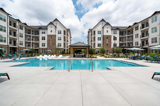 a swimming pool with chaise lounge chairs and umbrellas in front of an apartment building