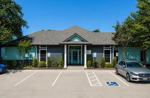 A parking lot in front of a building with a car parked in a handicap spot.