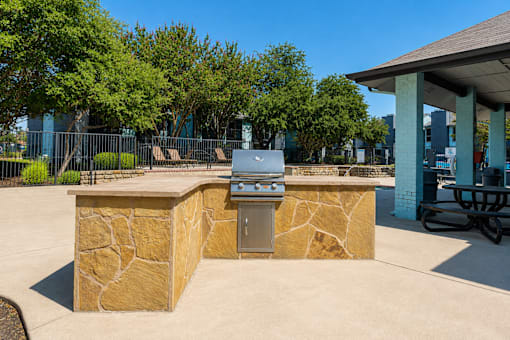 A stone barbecue grill is in the middle of a concrete patio.