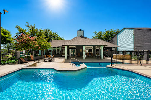 A pool in front of a house with a sunny sky.