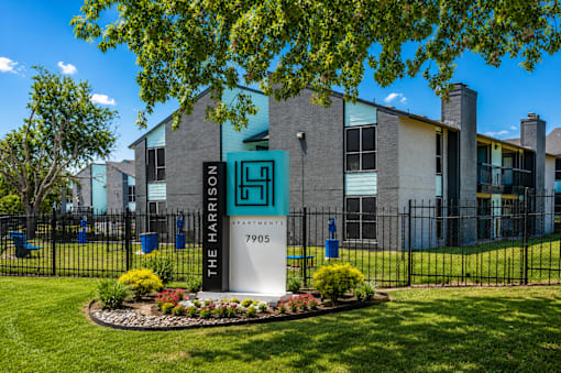 The Harris Apartments building is surrounded by a black fence and has a sign in front of it.