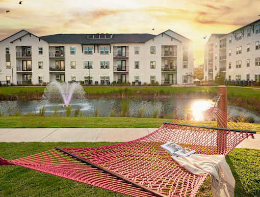 A red hammock is strung between two trees in a grassy area.