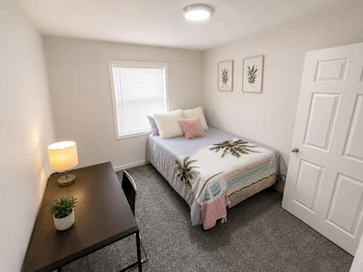 A bedroom with a bed, nightstand, and a plant.