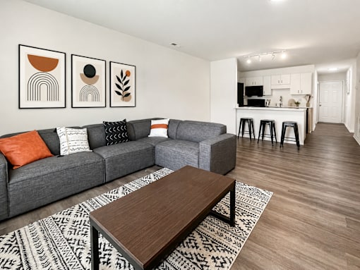 A living room with a grey couch, a coffee table, and a bar area in the background.