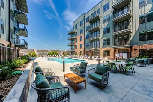 a pool with chairs and tables in front of an apartment building