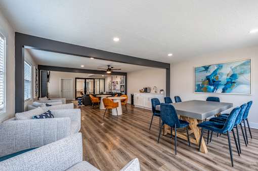 A modern living room with a grey sofa, a dining table with blue chairs, and a painting on the wall.