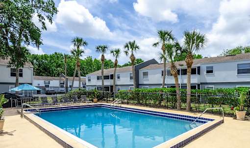 A swimming pool surrounded by palm trees and a building in the background.