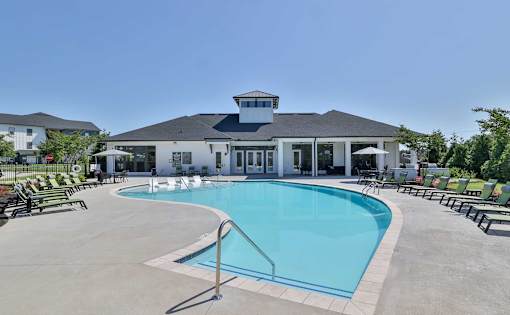 A large swimming pool in front of a building with a white facade and a black roof.