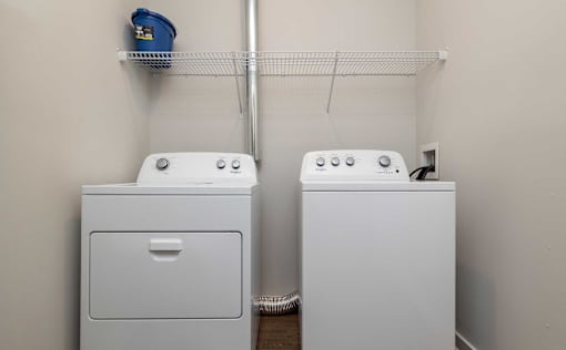 A laundry room with two washing machines and a shelf above them.